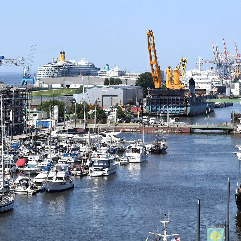 Weiter Ausblick über den Hafen mit großen Containerschiffen und kleinen Segelschiffen