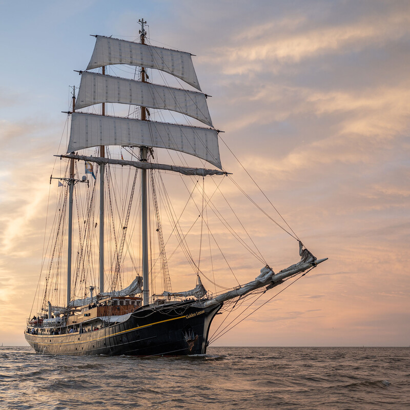 Segelschiff Gulden Leeuw auf dem Meer bei Sonnenuntergang. Abgebildet ist ein altes Segelschiff auf dunklem Wasser.