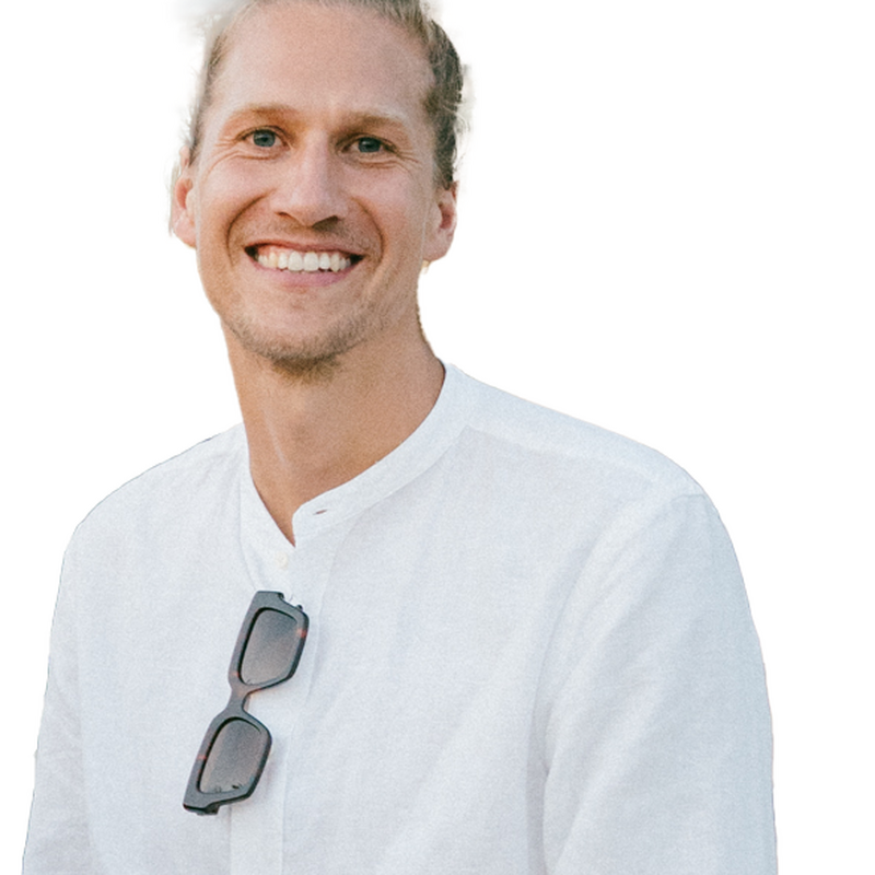 Portrait von Malte Ziegenhagen. Abgebildet ist ein Mann, der seine Hände in den Hosentaschen hat, eine Sonnenbrille an sein weißes Hemd gehängt und dabei in die Kamera lächelt.